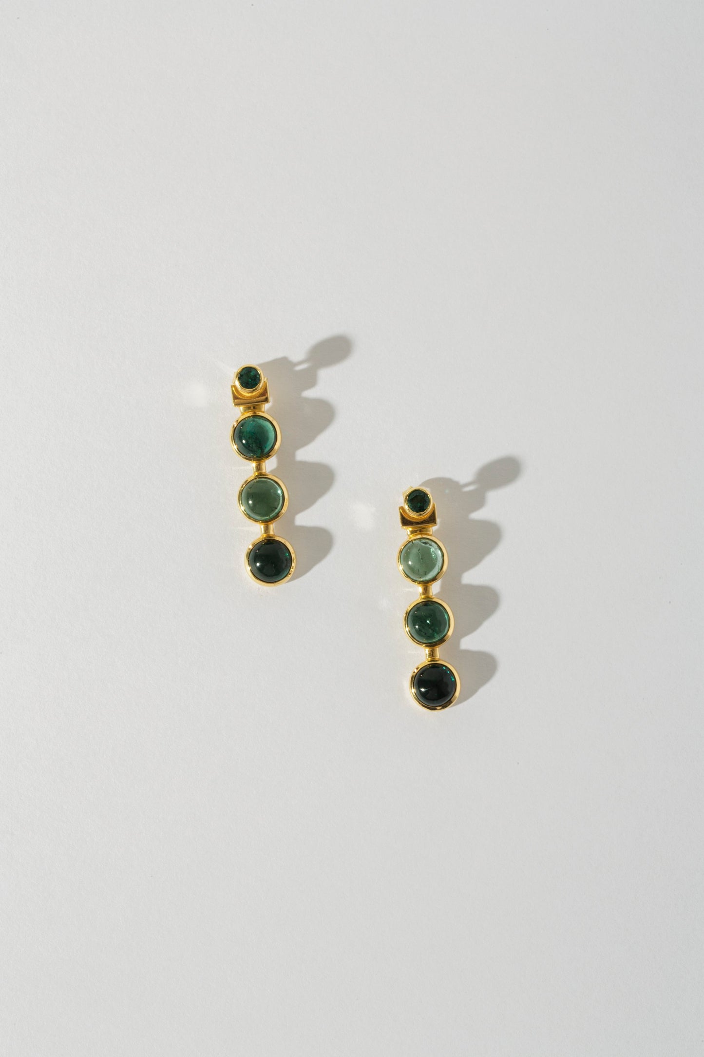 A pair of earrings with three tourmaline stones set in 18k yellow gold jackets, displayed against a white background.