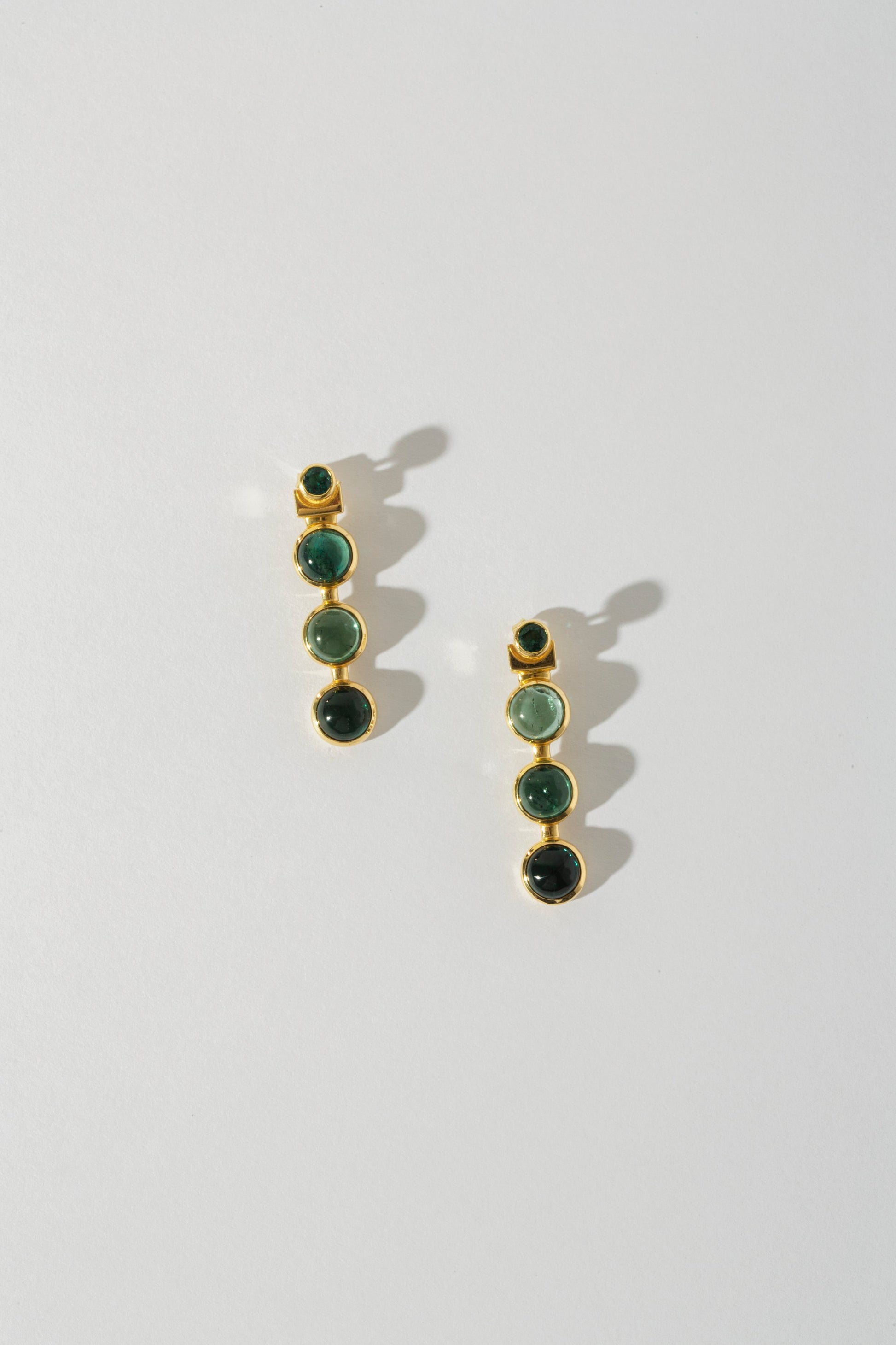 A pair of earrings with three tourmaline stones set in 18k yellow gold jackets, displayed against a white background.